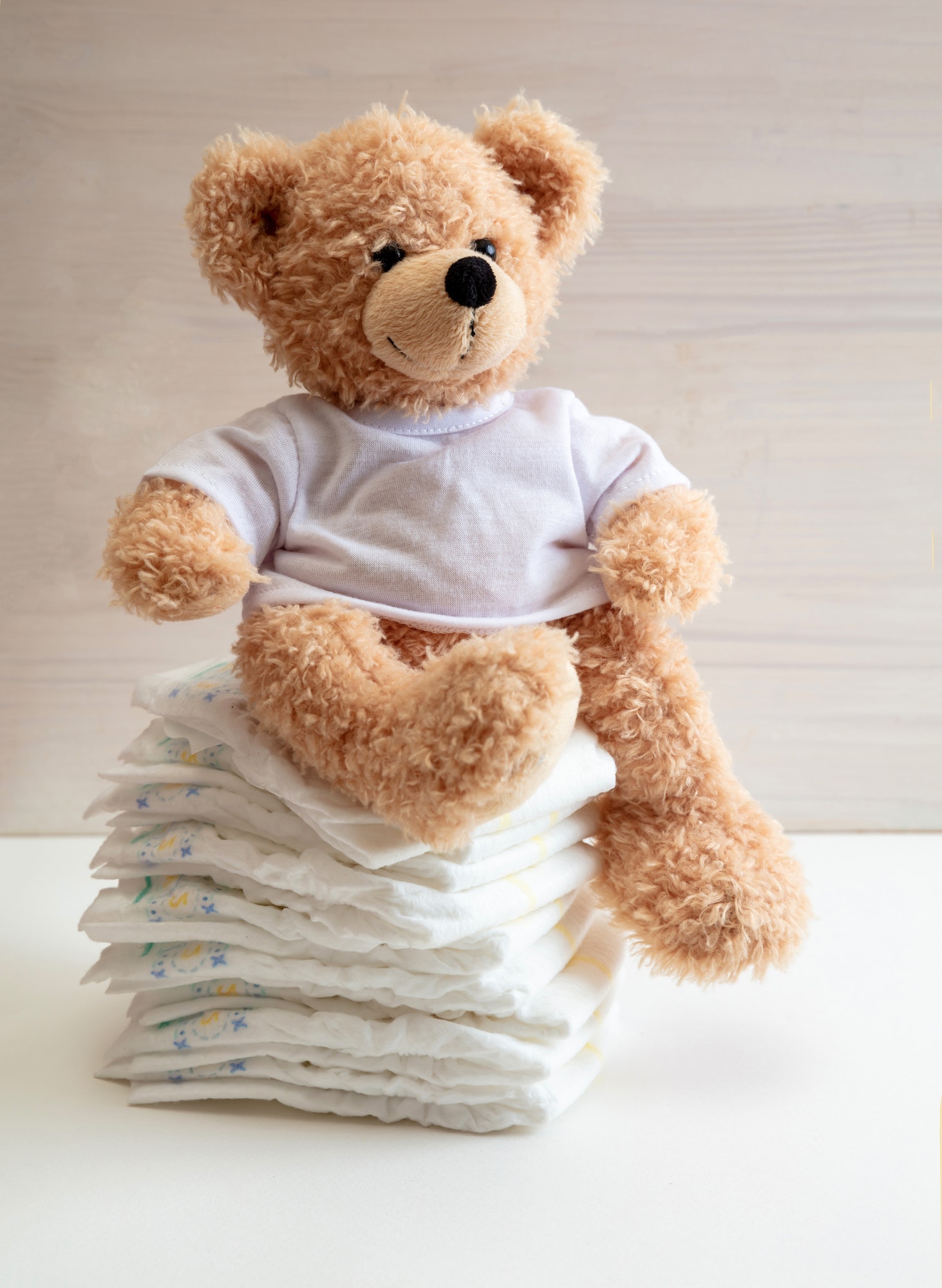 Baby diapers stack and teddy on white color floor